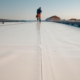 Image of a roofer working on a flat white roof.