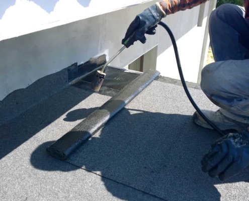 Roofer preparing part of bitumen roofing felt roll for melting by gas heater torch flam