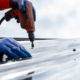 Roofer worker using air or pneumatic nail gun and installing metal sheet on top of the new roof