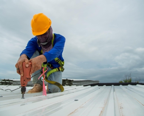Roofer drilling into white metal roof